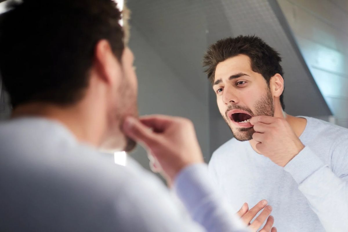 man looking at tooth in mirror