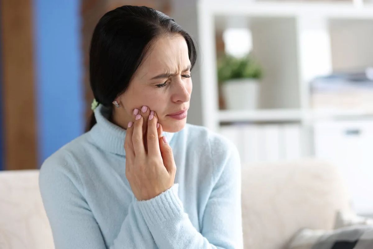 woman holding cheek in pain at home with toothache