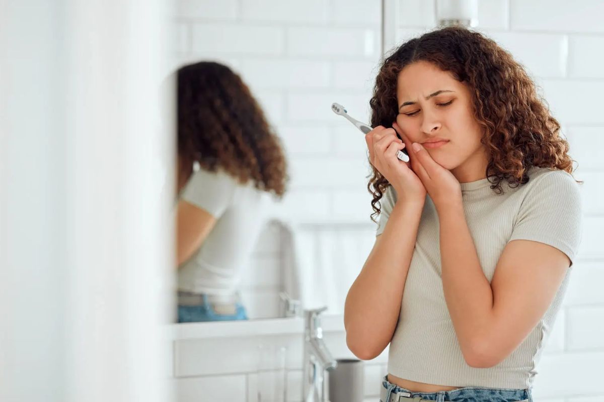 woman with toothache holding toothbrush in one hand and cheek with the other